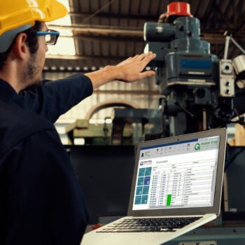 Man in hard hat looking at machine with laptop in front of him
