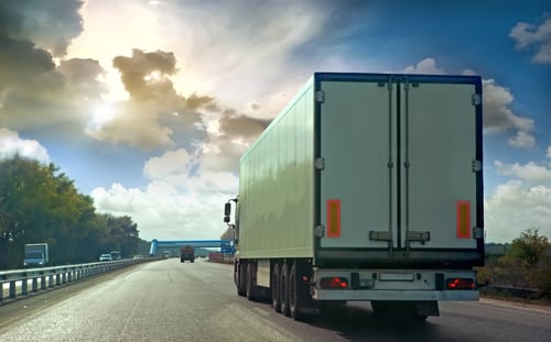 Delivery truck driving on road with cloudy skies in the background